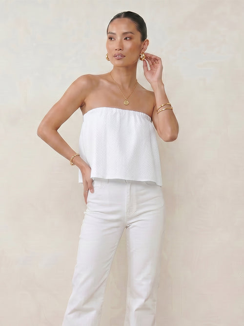 Model wearing the pearl white ruffle tube top with a floaty strapless summer silhouette against beige background