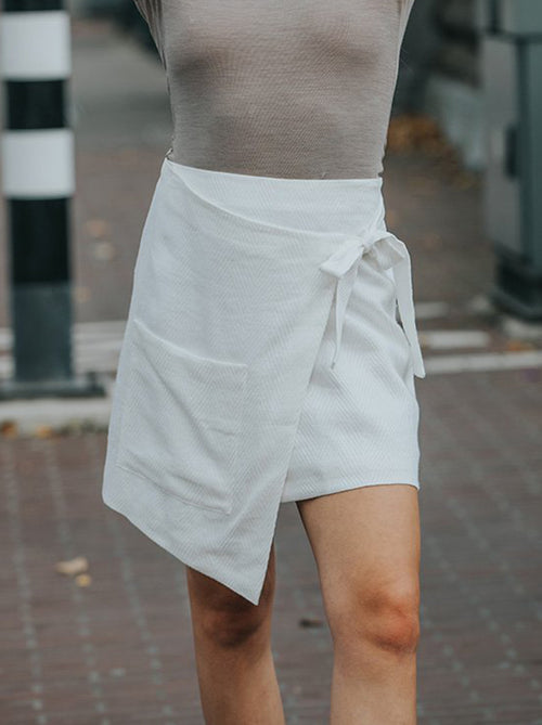 Model wearing the white asymmetric wrapped pocket skirt with attached belt and structured silhouette
