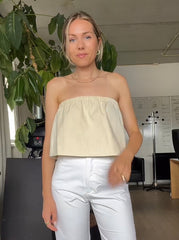 Model wearing an off white ruffle tube top, styled with white pants in a minimal indoor setting